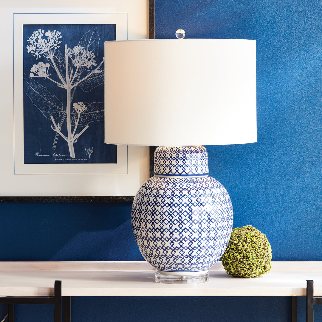 Chinoiserie blue and white ginger jar lamp with a white shade on a side table against a blue wall.