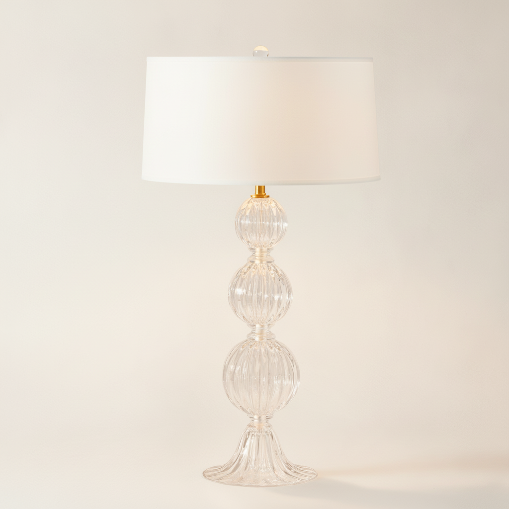 Decorative table lamp with a glass base and white shade on a neutral background