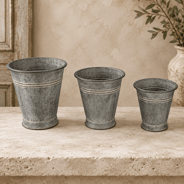 Metal bucket planter set showing aged surface texture, rolled rims, and horizontal bands.