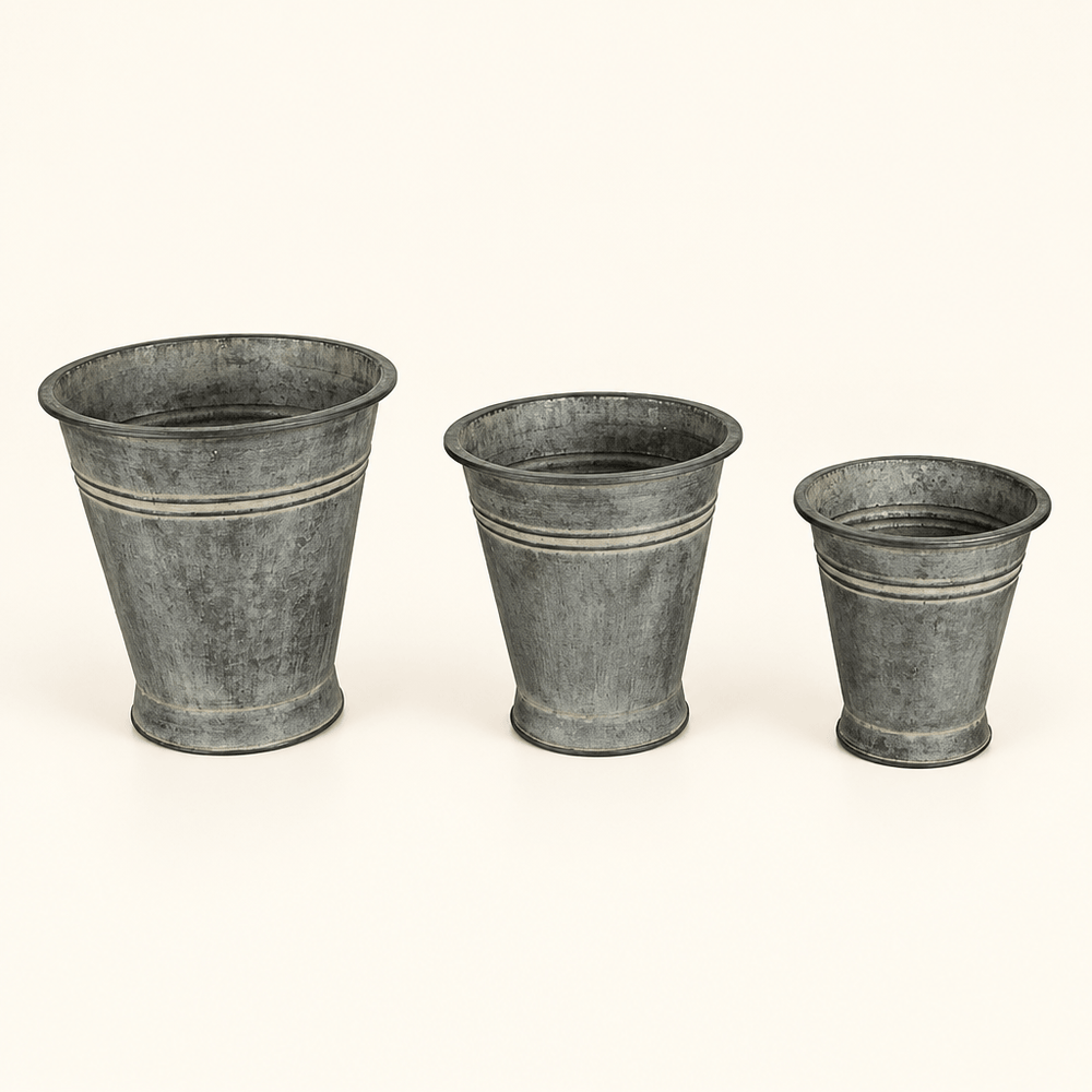 Three graduated metal bucket planters with tapered shapes and an aged finish on ivory.