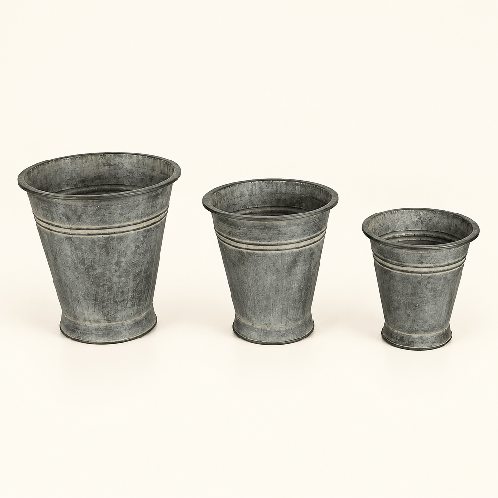 Three graduated metal bucket planters with tapered shapes and an aged finish on ivory.