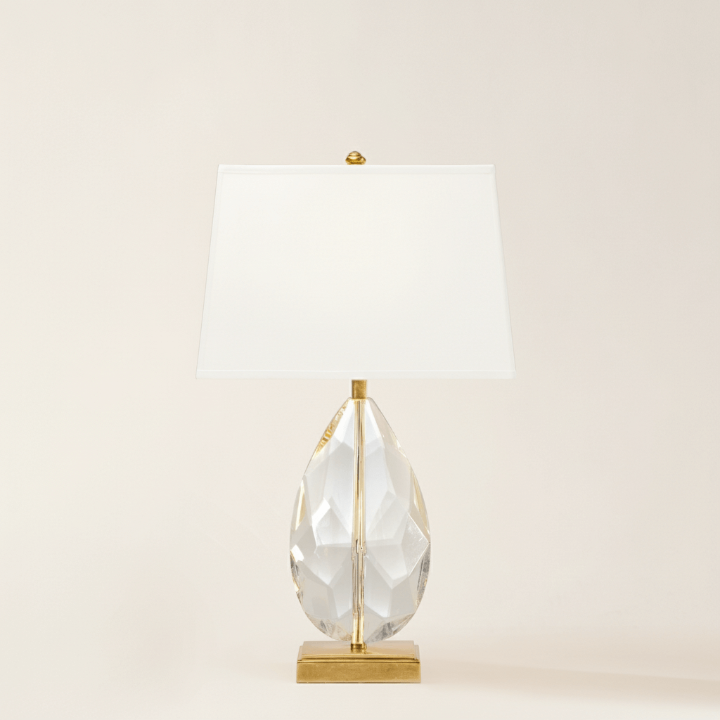 Table lamp with a clear glass base and gold accents on a beige background