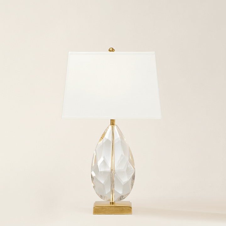Table lamp with a clear glass base and gold accents on a beige background