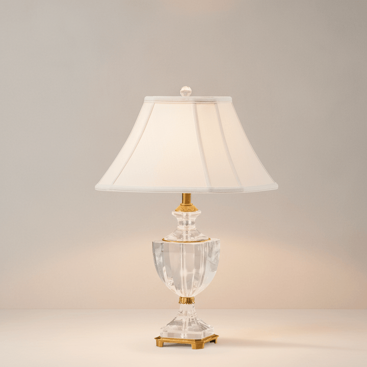 Decorative table lamp with a clear crystal glass base and white shade on a neutral background