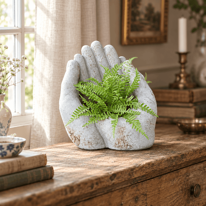 Cement cupped-hands planter with a fern on a wooden console near a cottage window