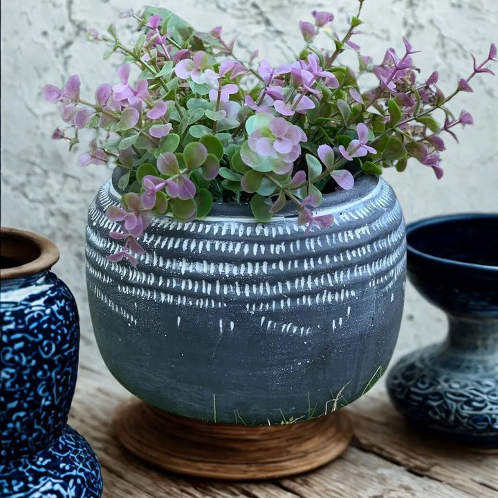 Dark glaze tribal relief planter styled with purple-green foliage on a wooden stand
