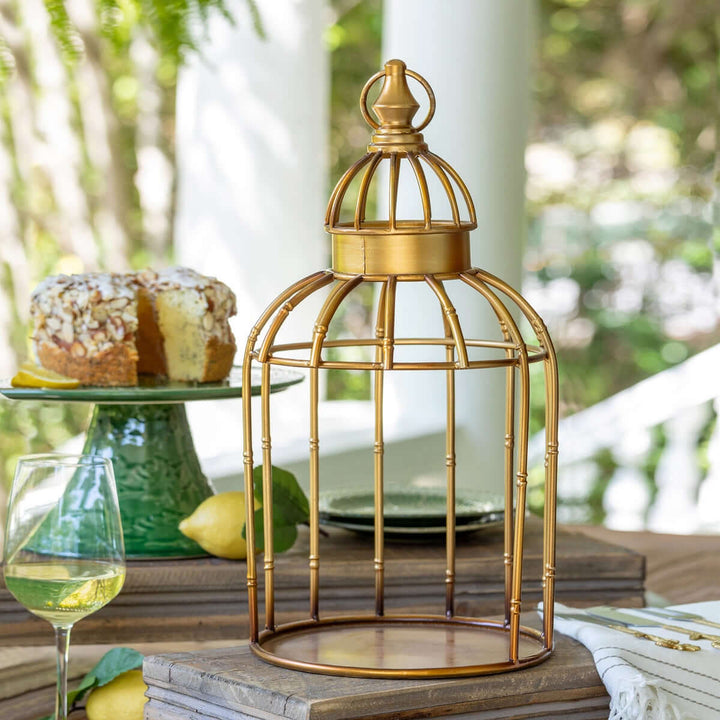 Vintage gold birdcage centerpiece stand on a wooden table with lemons and wine in an outdoor setting.