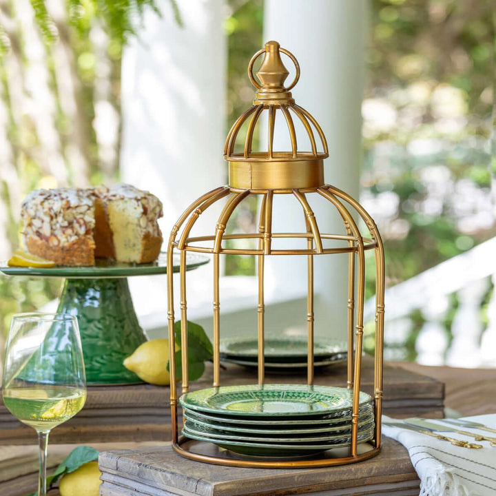 Decorative vintage gold birdcage centerpiece stand on table with green plates and cake, perfect for elegant home décor.