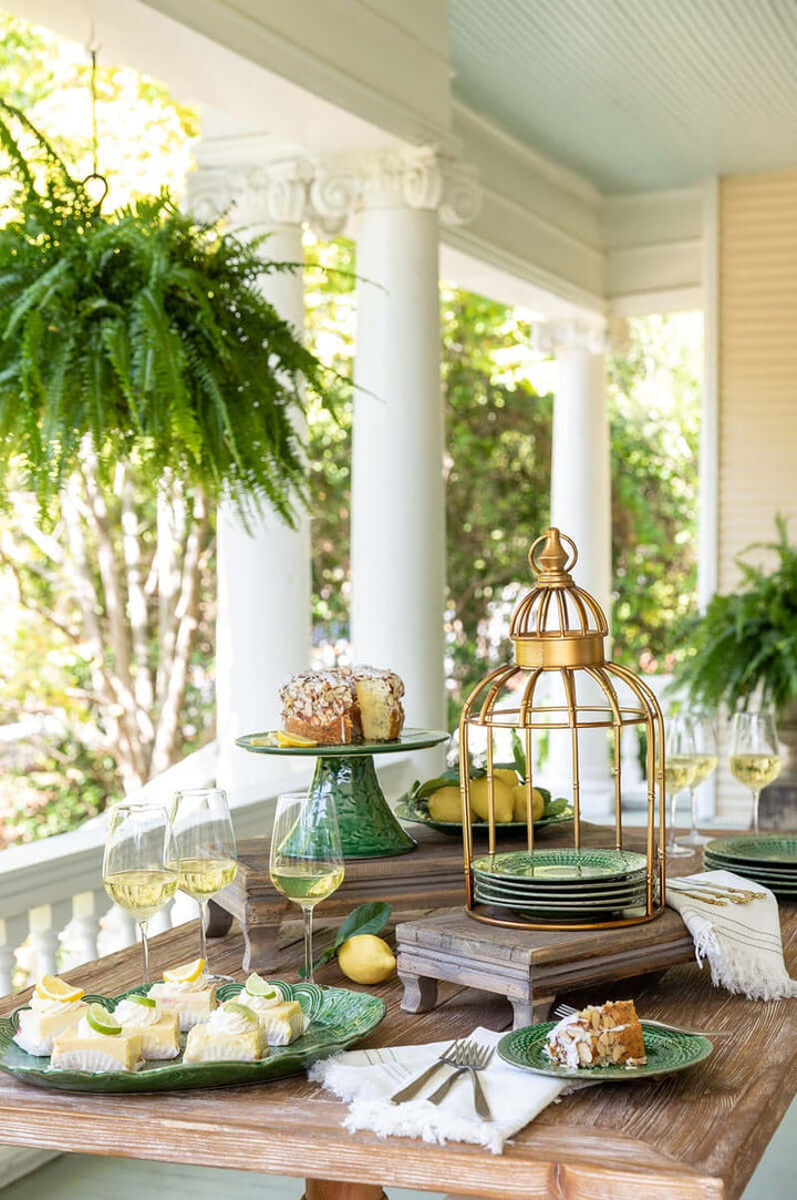 Vintage gold birdcage centerpiece stand on outdoor table with desserts and greenery, evoking antique home décor charm.