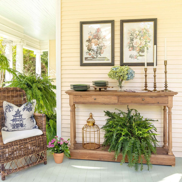 Charming porch with wicker chair, decorative vintage gold birdcage centerpiece, and floral artwork, creating a cozy atmosphere.