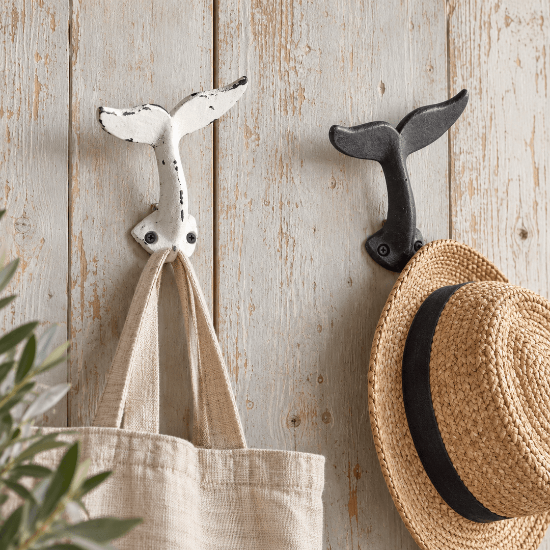 White and black whale tail wall hooks holding a linen tote and straw hat in a coastal entry