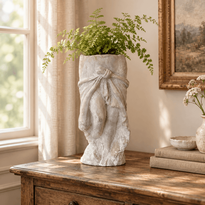 Draped skirt cement planter styled with a fern on a wooden console beside a window