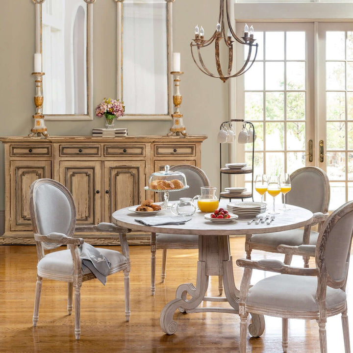 Elegant French country dining room with antique table, upholstered chairs, and rustic sideboard.