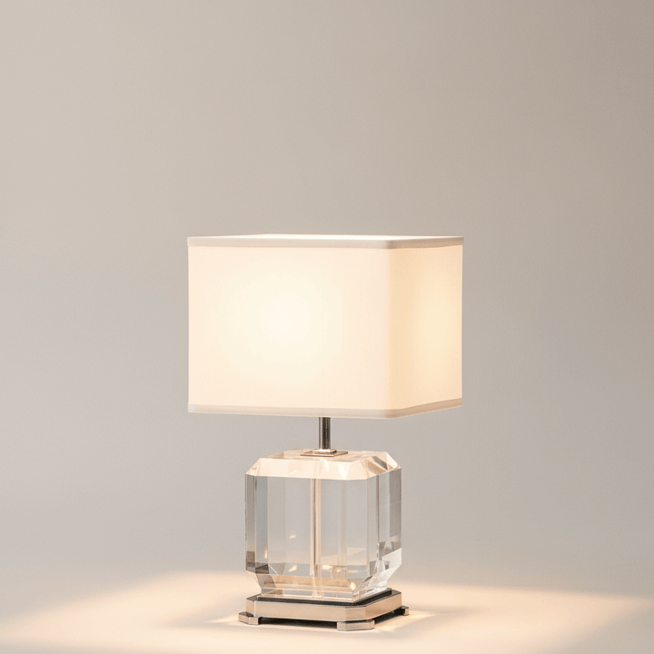 Table lamp with a clear glass base and white fabric shade on a gray background