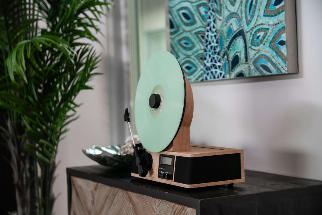 Turntable with a green vinyl record on a wooden turntable in a room with a peacock feather painting.