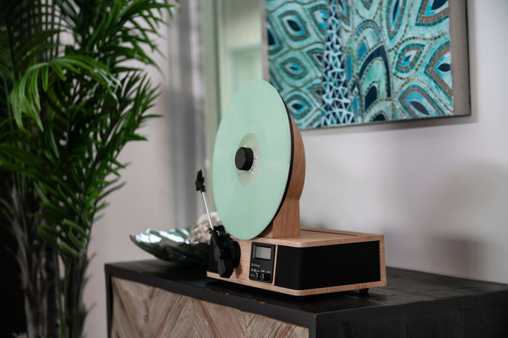 Turntable with a green vinyl record on a wooden turntable in a room with a peacock feather painting.