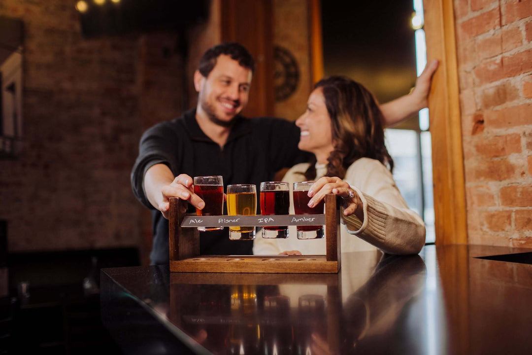 Couple enjoying tasting with Rustic Craft Beer Flight Tasting Set on a handcrafted acacia wood tray at a cozy bar.
