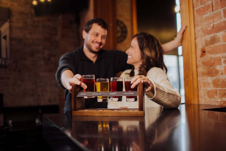 Couple enjoying tasting with Rustic Craft Beer Flight Tasting Set on a handcrafted acacia wood tray at a cozy bar.