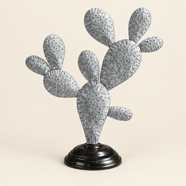 Galvanized prickly pear cactus sculpture with pressed silver pads and a black round base on an ivory background.