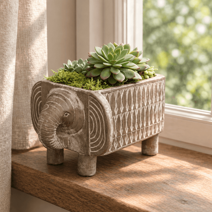 Geometric resin elephant planter holding succulents on a wooden windowsill beside a linen curtain