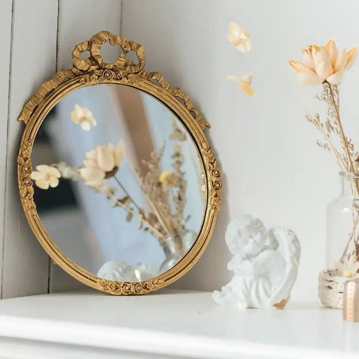 Gilded bow and rose oval wall mirror leaning on a bright mantel
