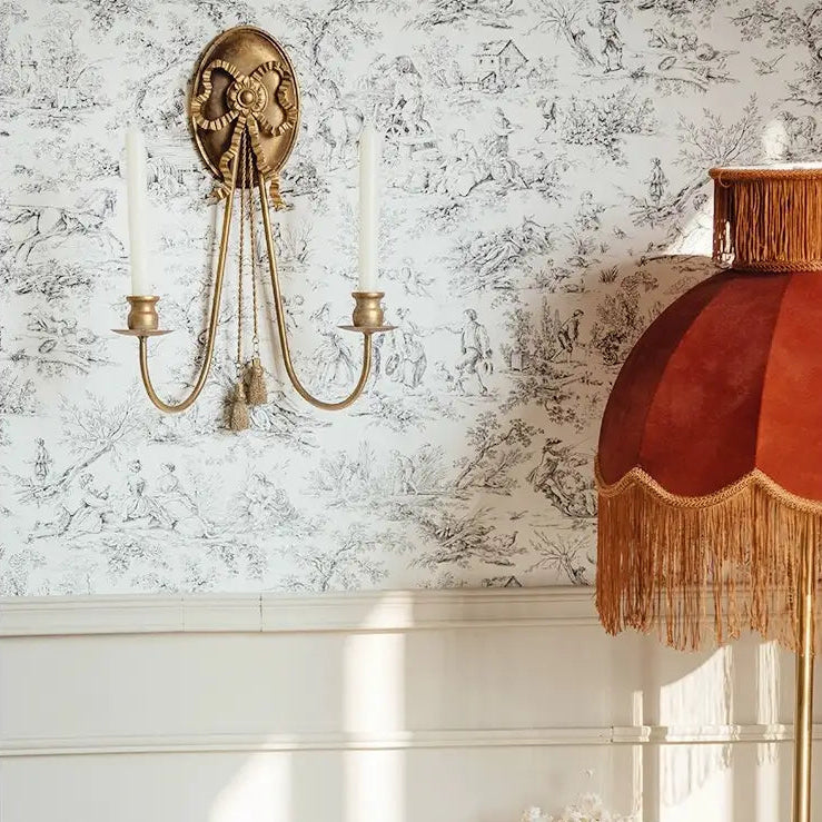 Two-light wall sconce with bow and tassels against toile wallpaper
