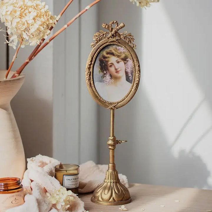 Gilded pedestal oval photo frame styled with flowers and a portrait in soft window light