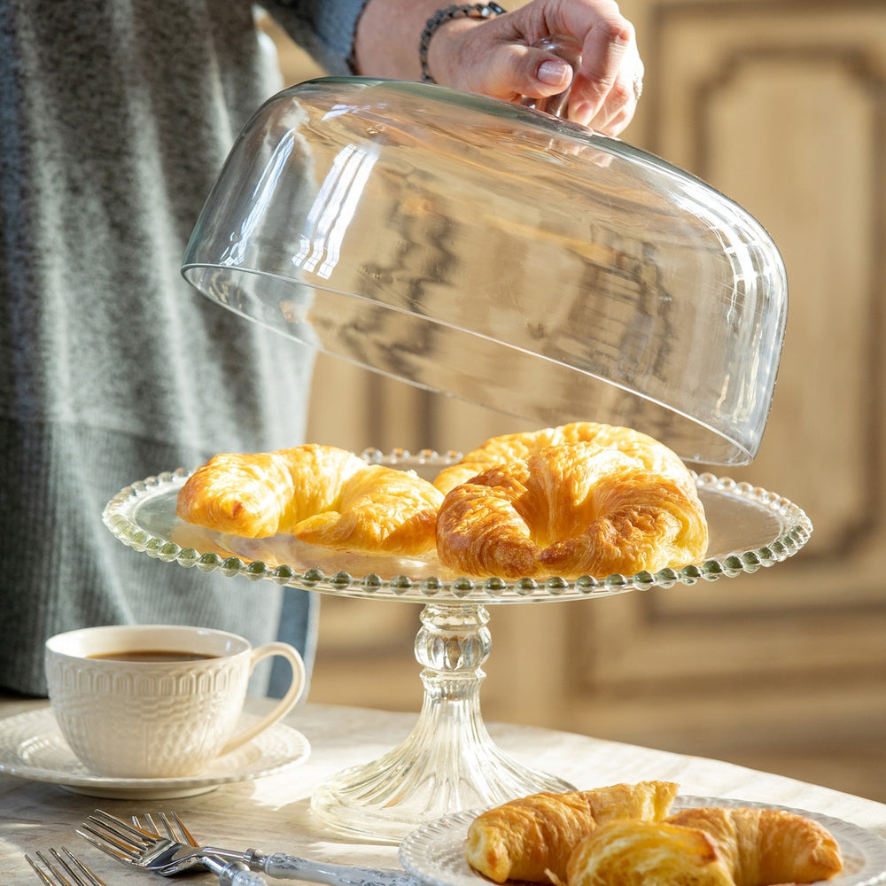 Glass Cake Stand with Dome and Beaded Edge Pedestal Plate showcasing croissants on a table setting with coffee.