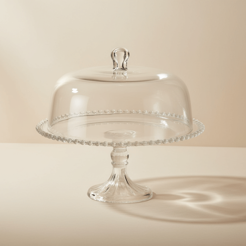 Clear glass cake stand with dome lid on a beige background