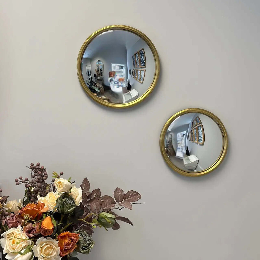 Two sizes of gold-framed convex mirrors reflecting a wide-angle room view