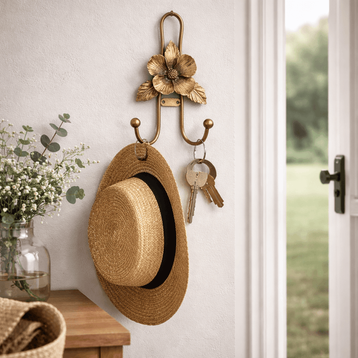 Gold iron flower wall hook holding a straw hat and keys beside an entryway door