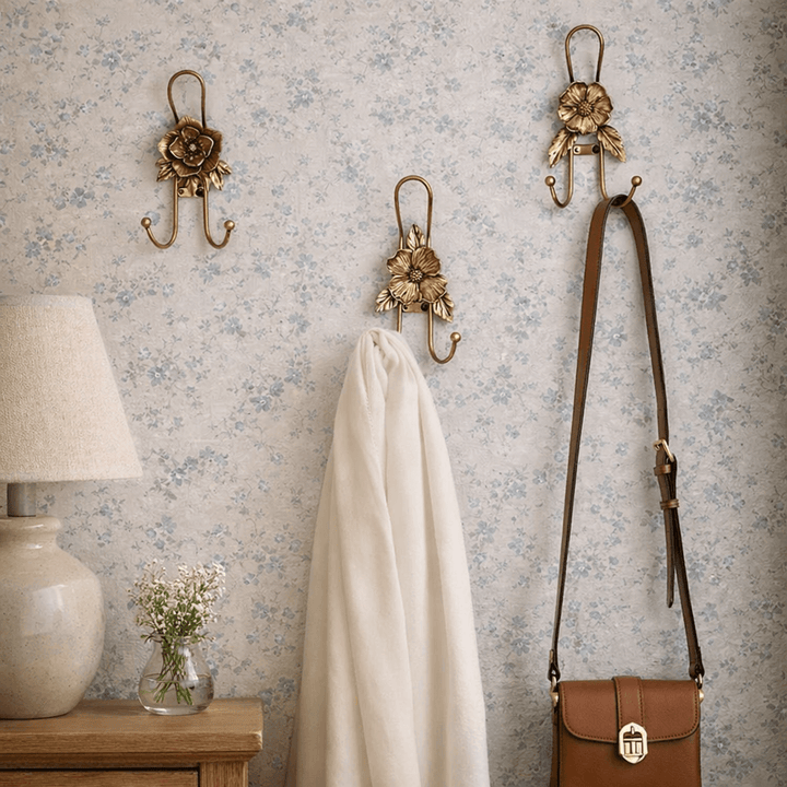 Three gold iron flower wall hook styles holding a scarf and handbag on floral wallpaper