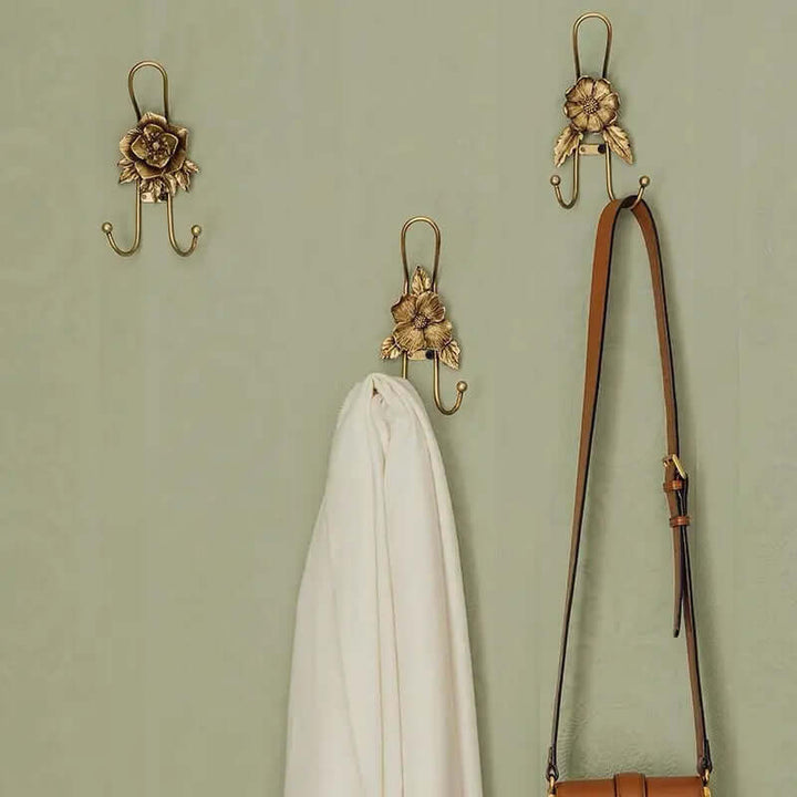 Three floral styles of gold iron wall hooks arranged on a sage green wall