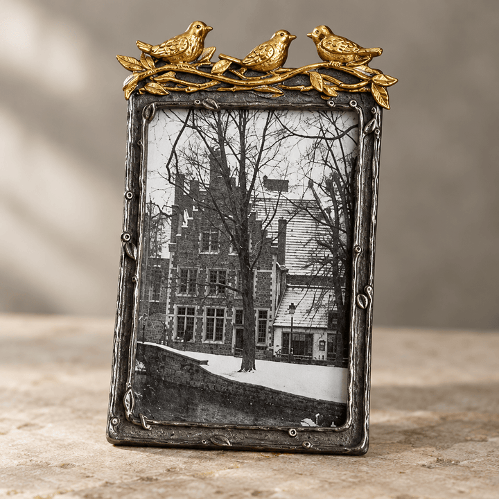 Close detail of gold-leaf bird accents and the textured branch-like pewter border of a vertical photo frame.