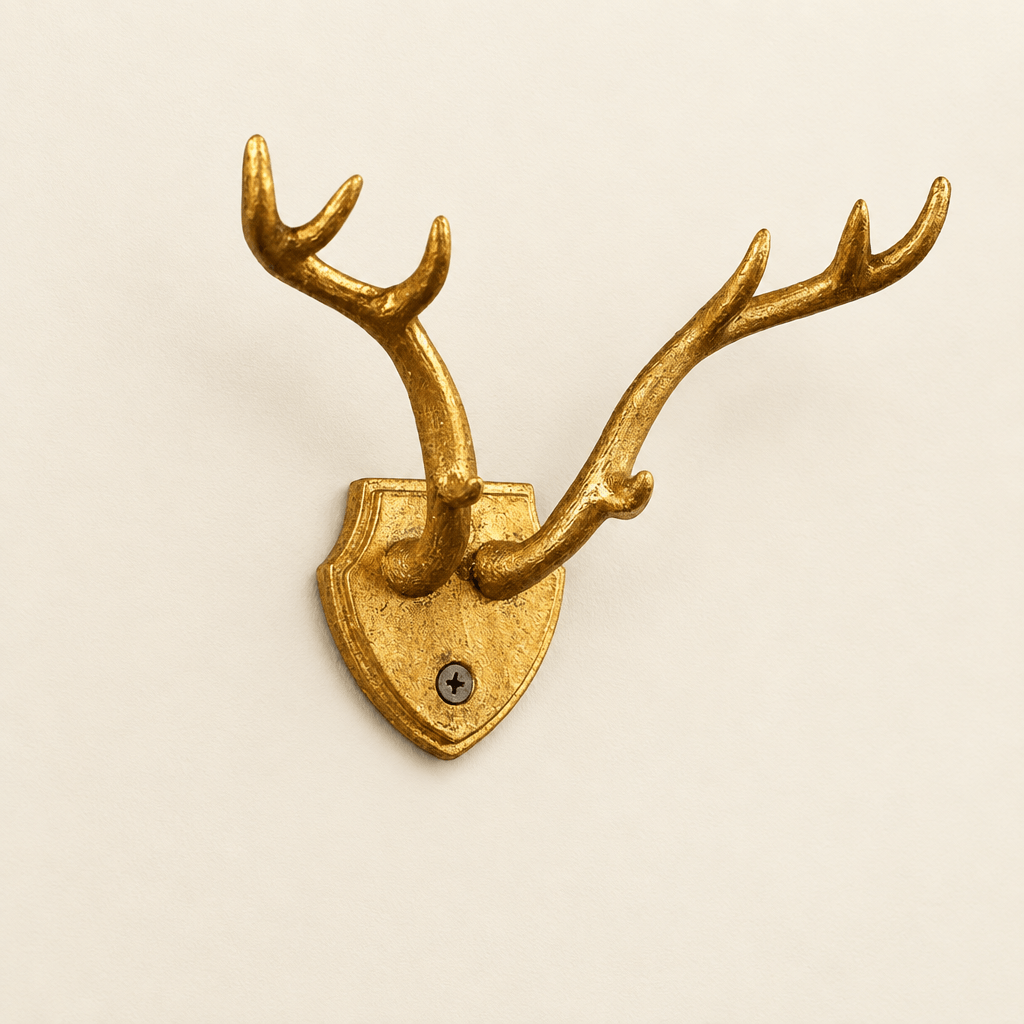Gold-leaf cast iron antler wall hook with a shield-shaped backplate against an ivory wall.