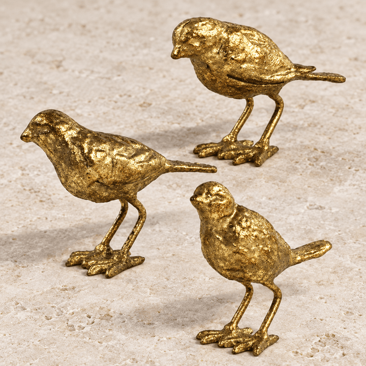 Gold-leaf cast iron bird figurines on pale stone showing textured feathers and distinct poses.