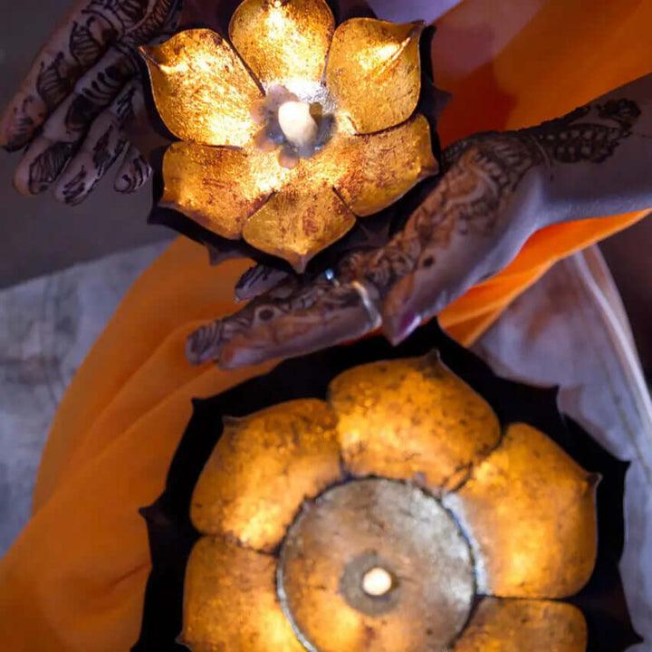 Gold-leaf lotus candle bowl glowing with a central candle and shown in hand for scale