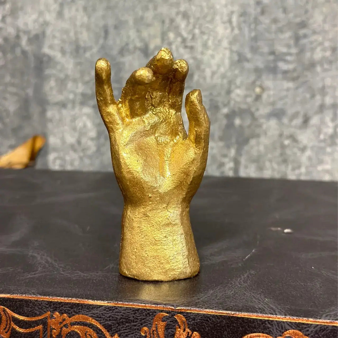 Two Gold Leaf Pewter Blessing Hand Figurine styles on a dark shelf