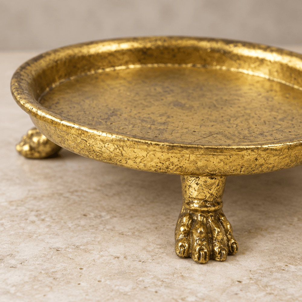 Close-up of a sculptural claw foot, curved rim, and textured gold-leaf finish on a pewter dish.