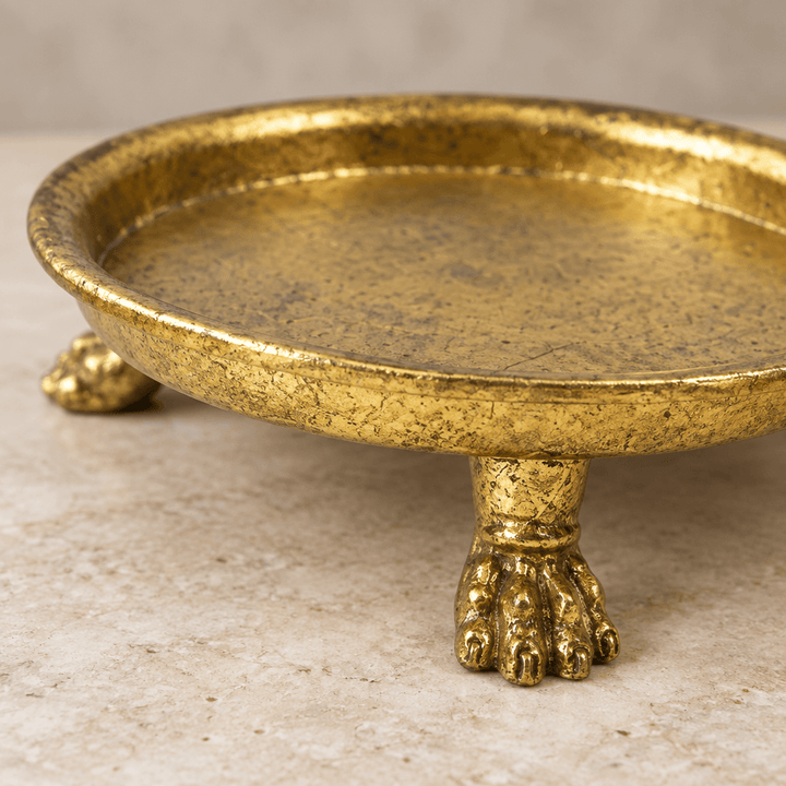 Close-up of a sculptural claw foot, curved rim, and textured gold-leaf finish on a pewter dish.