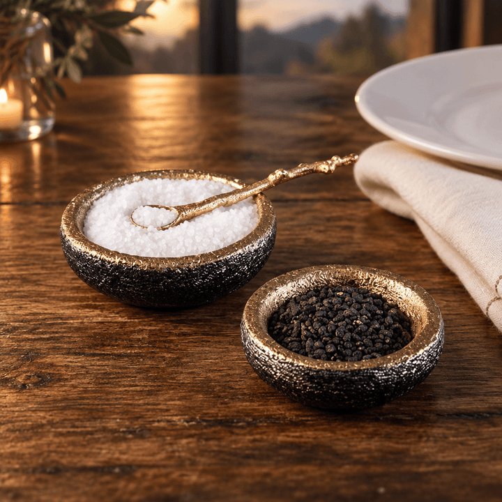 Gold salt and pepper cellar set with one spoon on a wooden dining table beside ivory linen