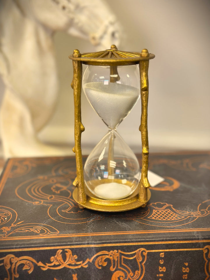 Golden branch hourglass with white sand displayed on a richly patterned book