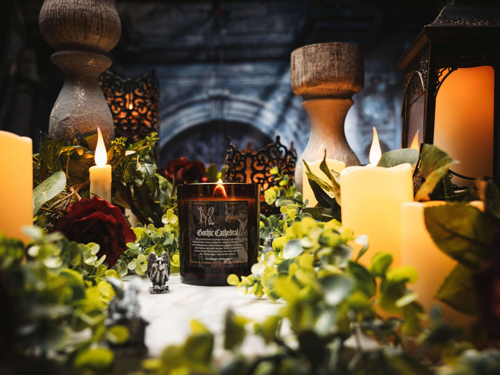 Gothic Cathedral Candle surrounded by foliage and lit candles in a medieval-inspired setting.
