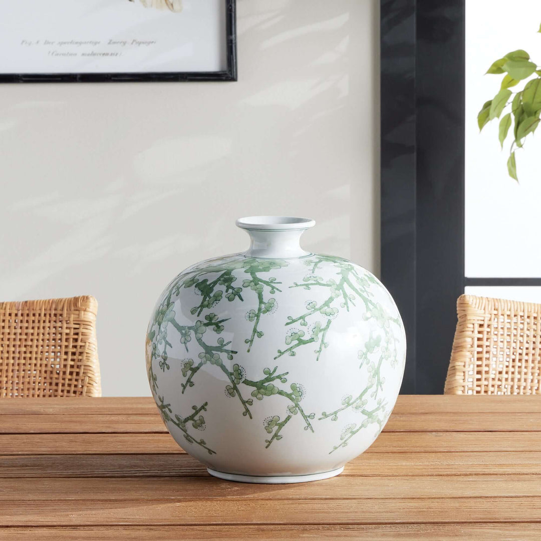 Green and white chinoiserie porcelain vase with hand-painted plum blossoms, styled on a wooden table with a serene backdrop.