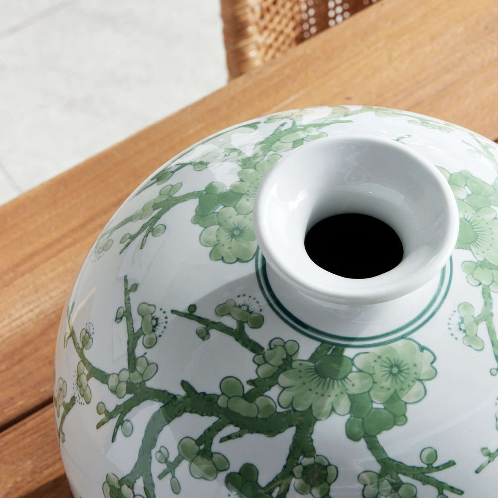 Round porcelain vase with green plum blossom design on a wooden table, evoking vintage European and Eastern artistry elegance.