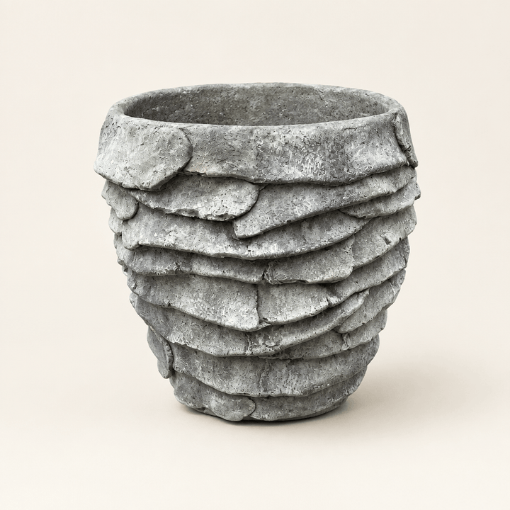 Grey cement palm leaf planter with overlapping leaf relief on an ivory studio background