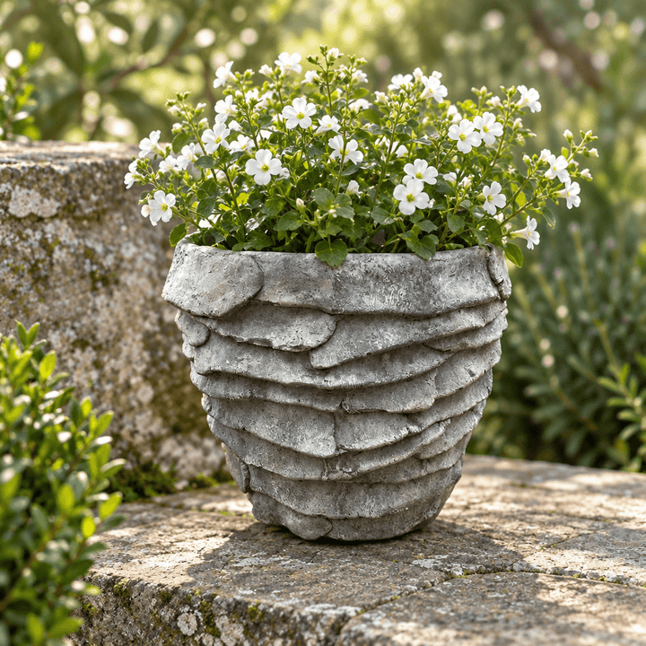 Grey cement palm leaf planter styled with white flowers on a weathered stone garden terrace