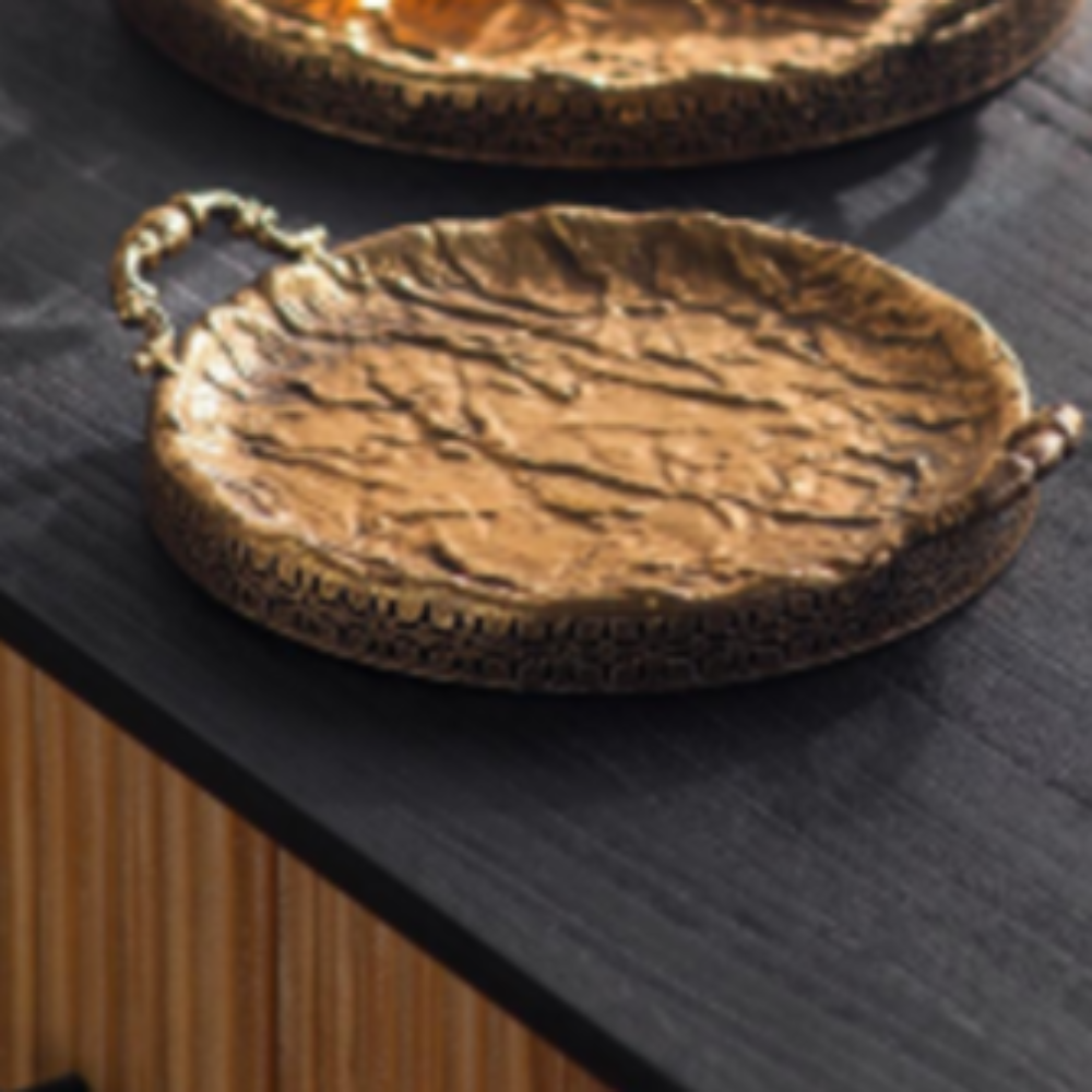 Close view of a hammered antique gold round serving tray with ornate handles