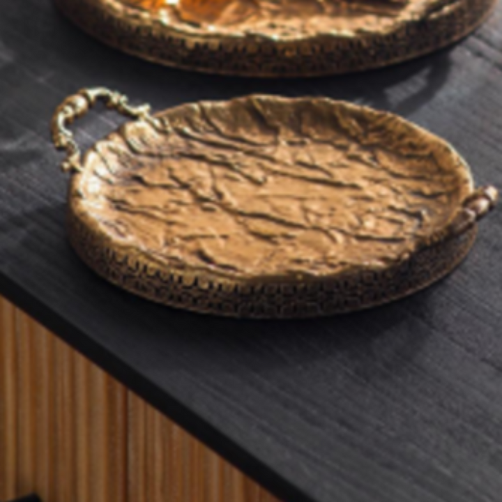 Close view of a hammered antique gold round serving tray with ornate handles