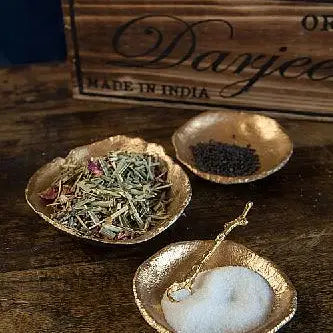 Three small gold condiment dishes with herbs, seasoning, and a spoon